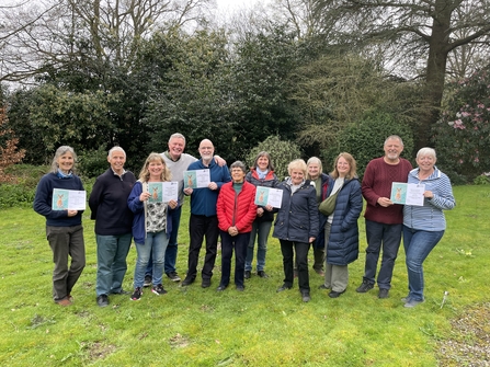 Twelve people stood in a green garden holding certificates. 