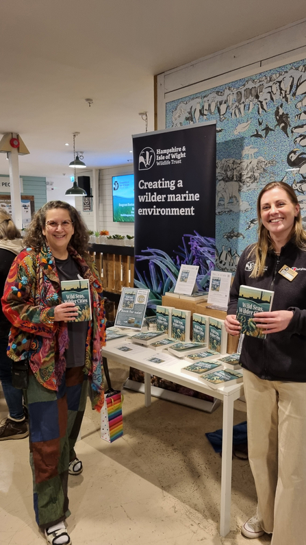 Two people stood holding books, smiling at the camera. 
