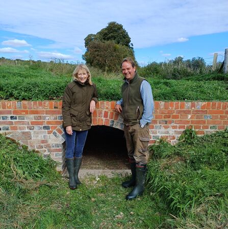 Two people smiling and standing in front of a newly repaired brick cart bridge