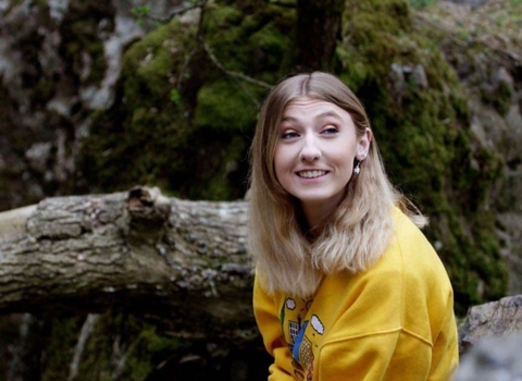 Georgina sat in the wood, smiling, looking off into the distance