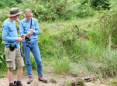 two members of staff in teal uniform looking at species collection cup  