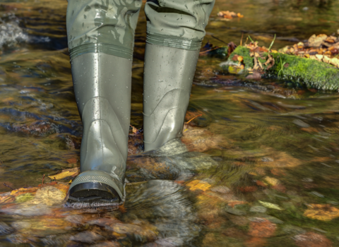 Person walking through river in waders. Image shows waders in clear river water.