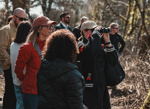 A group of people along a woodland path. One is looking out with binoculars