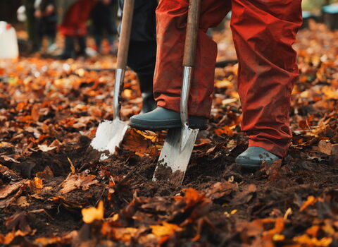 2 spades being pushed into the ground by children wearing wellies