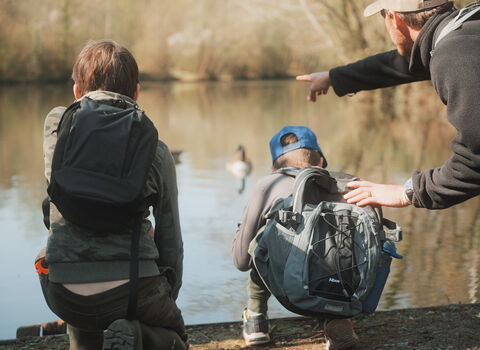 2 teenagers looking out over a pond with an adult pointing out something in the water